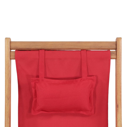 Close-up of a red fabric seat and wooden frame of a folding beach chair with a matching headrest.