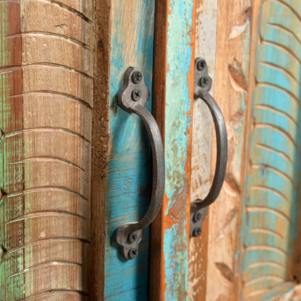 Close-up of reclaimed wood cabinet door with ornate metal handles and colorful painted details.