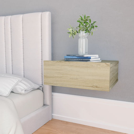 Floating nightstand in Sonoma oak finish with integrated drawer, styled with a vase and books beside a bed.