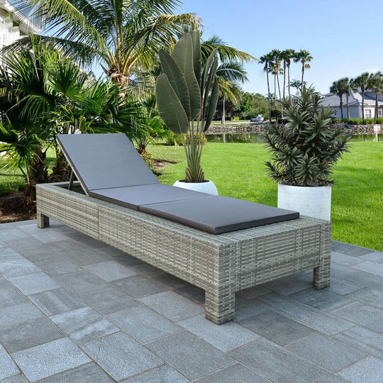 Stylish grey poly rattan sunbed with cushion, perfect for relaxing by the pool or on the patio, surrounded by lush greenery.