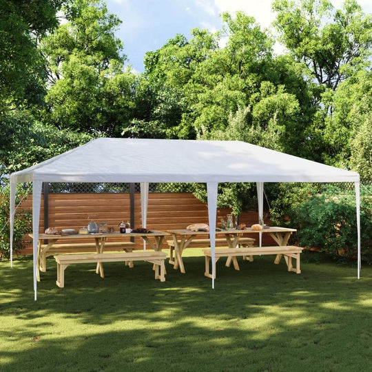 Party tent 4x6 m white set up outdoors with wooden benches and tables, surrounded by lush greenery. Ideal for outdoor gatherings.