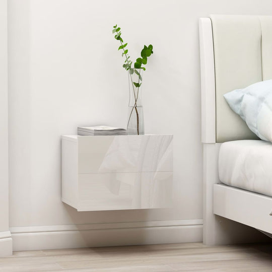 High gloss white bedside cabinet with two drawers and decorative plant, beside a modern bed setting.