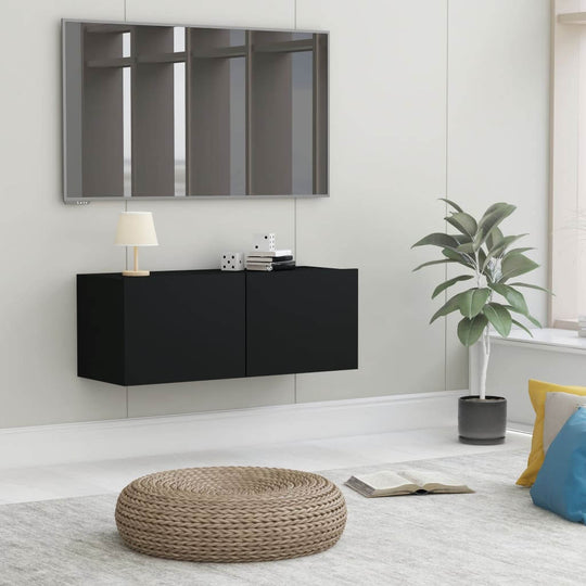 Stylish black TV cabinet with drop-down doors, mirrored wall, and decorative plant in a modern lounge setting.