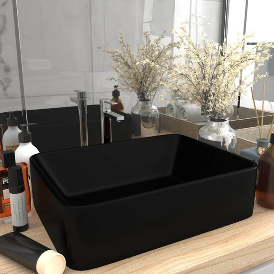 Luxury matt black ceramic wash basin on a wooden countertop, surrounded by bathroom accessories and decor.