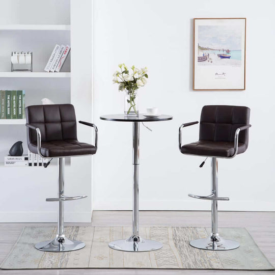 Two modern brown faux leather bar stools with a chrome base and a round table in a stylish indoor setting.