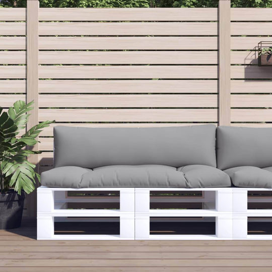 Gray outdoor pallet cushions on a white wooden frame, set in a garden patio with a privacy fence and greenery.