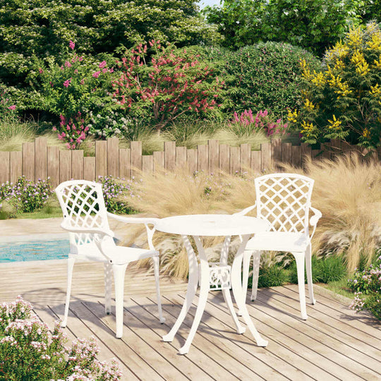 Elegant 3 piece white cast aluminium bistro set on a patio surrounded by lush greenery and flowers. Ideal for outdoor use.