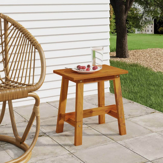 Rectangular solid acacia wood stool placed beside a chair on a patio, ideal for outdoor living spaces and garden furniture.