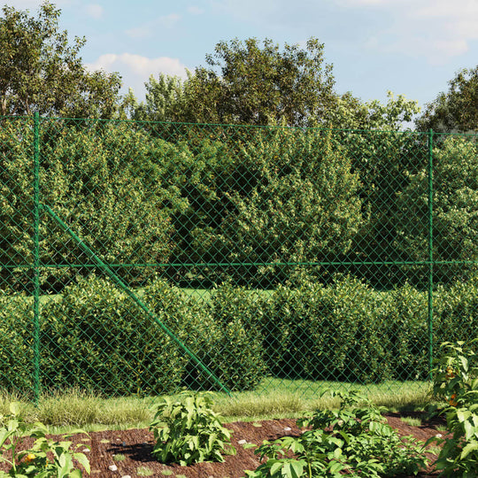 Green chain link fence with spike anchors surrounding lush greenery and plants, providing security and enclosure.