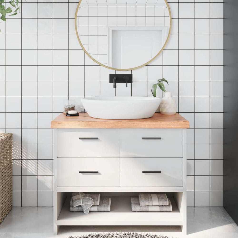 Stylish bathroom vanity with light brown solid wood countertop, white basin, and modern mirror against a tiled wall.