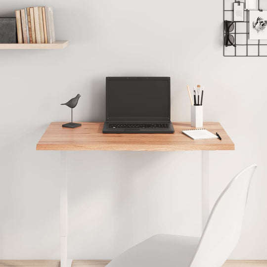 Modern desk setup with laptop, notebook, and decorative items on light brown wood tabletop and white chair.