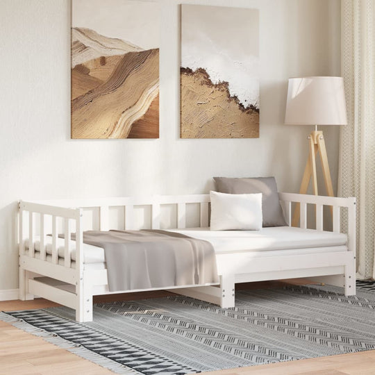 White wooden pull-out day bed in a cozy living room setting, featuring slatted design and decorative pillows on a patterned rug.