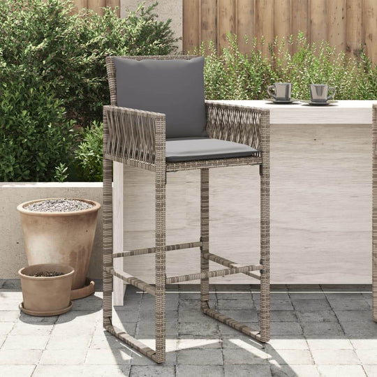 Grey poly rattan garden bar stool with cushion beside a patio table in a landscaped outdoor space.