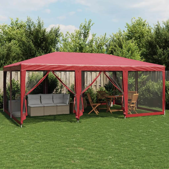 Red party tent with 10 mesh sidewalls, outdoor furniture area including lounge sofa and dining set, surrounded by greenery.